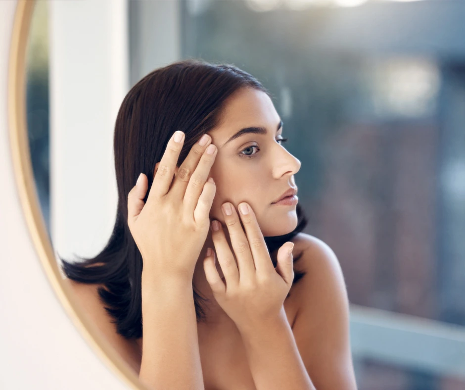 Medical dermatology: Woman examining her skin closely in front of a round mirror indoors